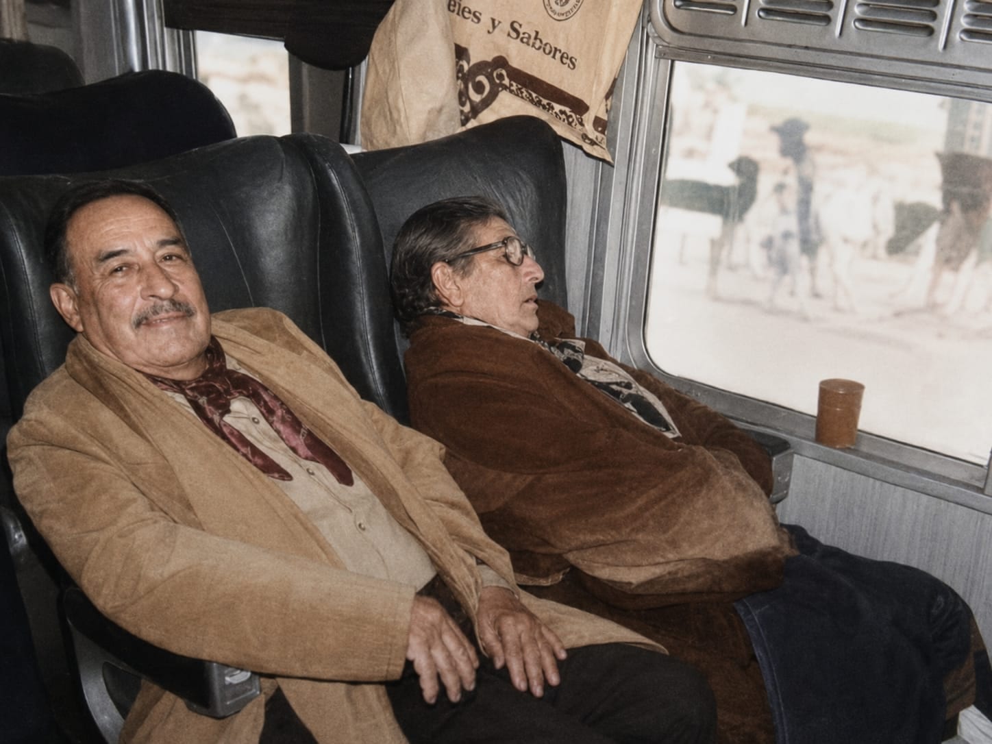 Fotografía original: dos hombres mayores viajando sentados, uno mirando a cámara y el otro dormido contra la ventanilla